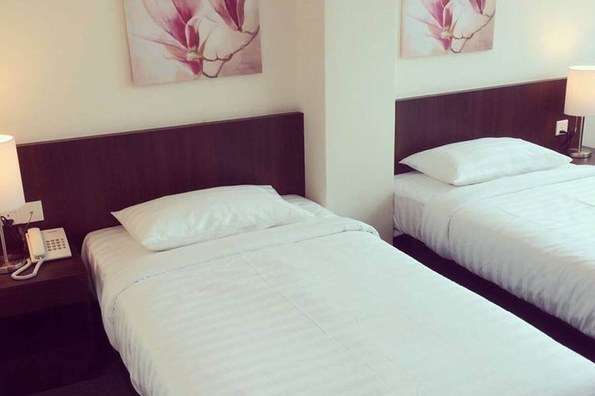 Two single beds with white linens, a wooden headboard, a bedside telephone, and a wall-mounted lamp.