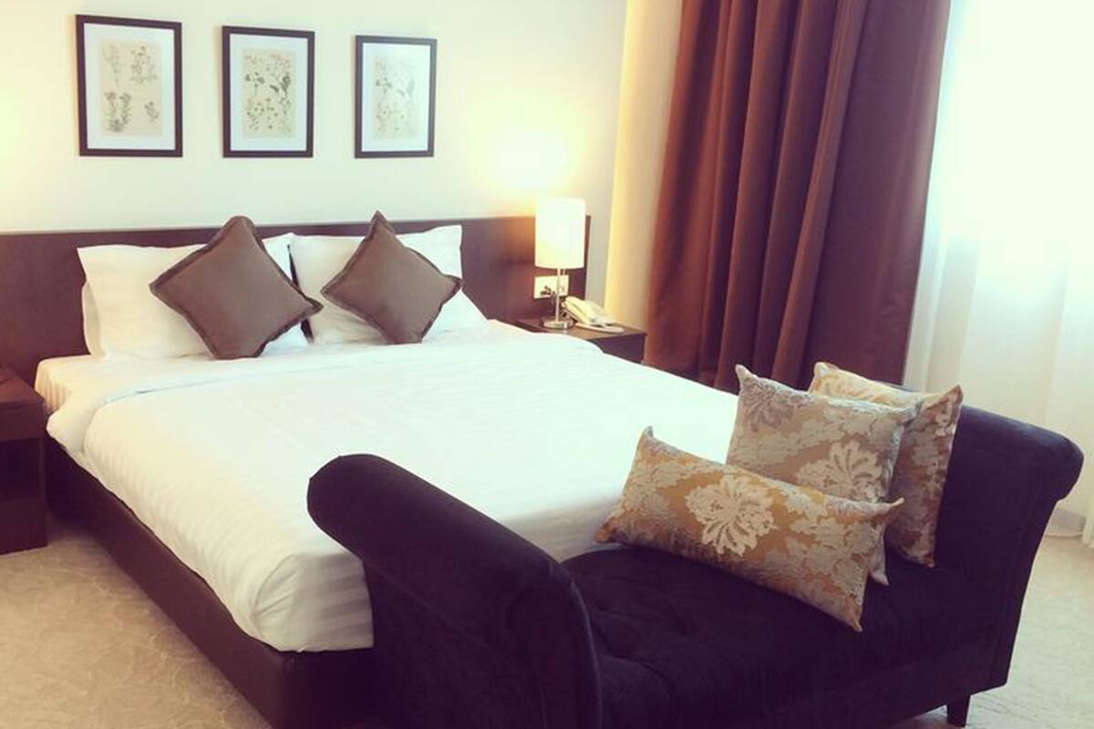 A hotel room with a large bed, a nightstand, a lamp, and a chair. There are three framed pictures on the wall.