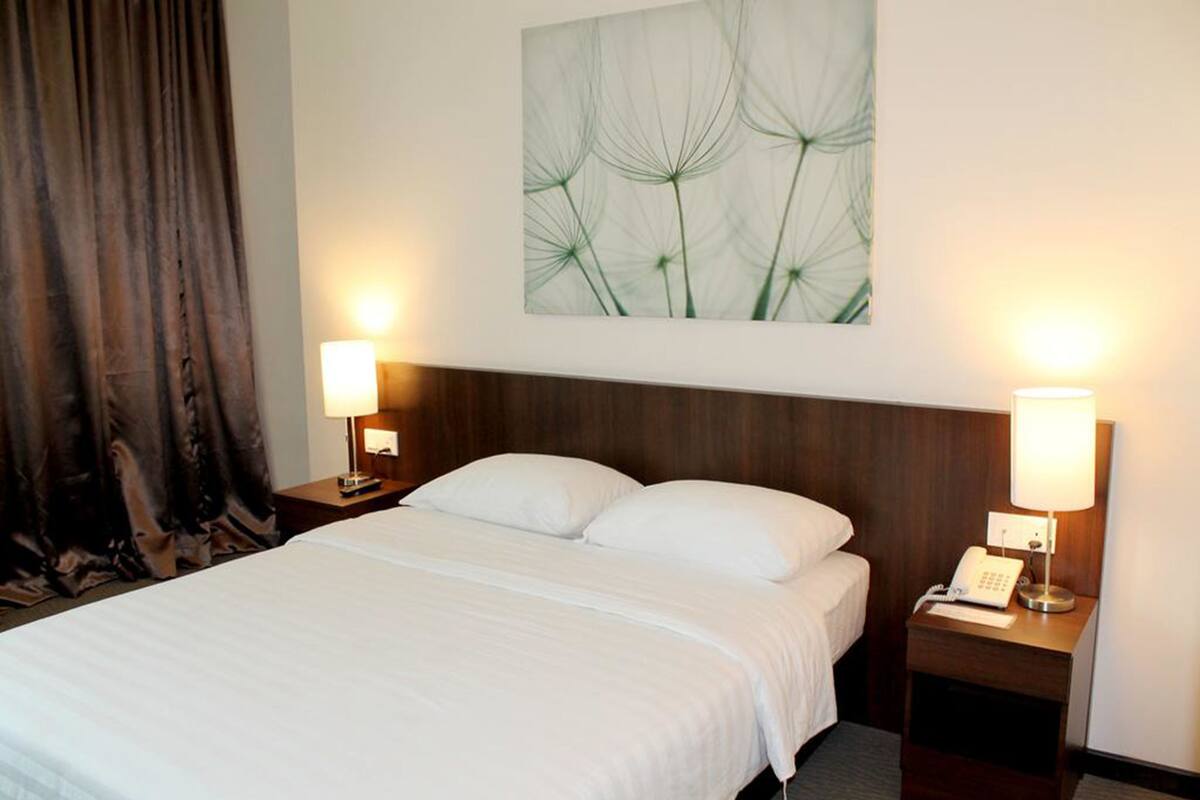 A hotel room with a large bed, two bedside tables with lamps, a telephone, and a wall-mounted artwork.