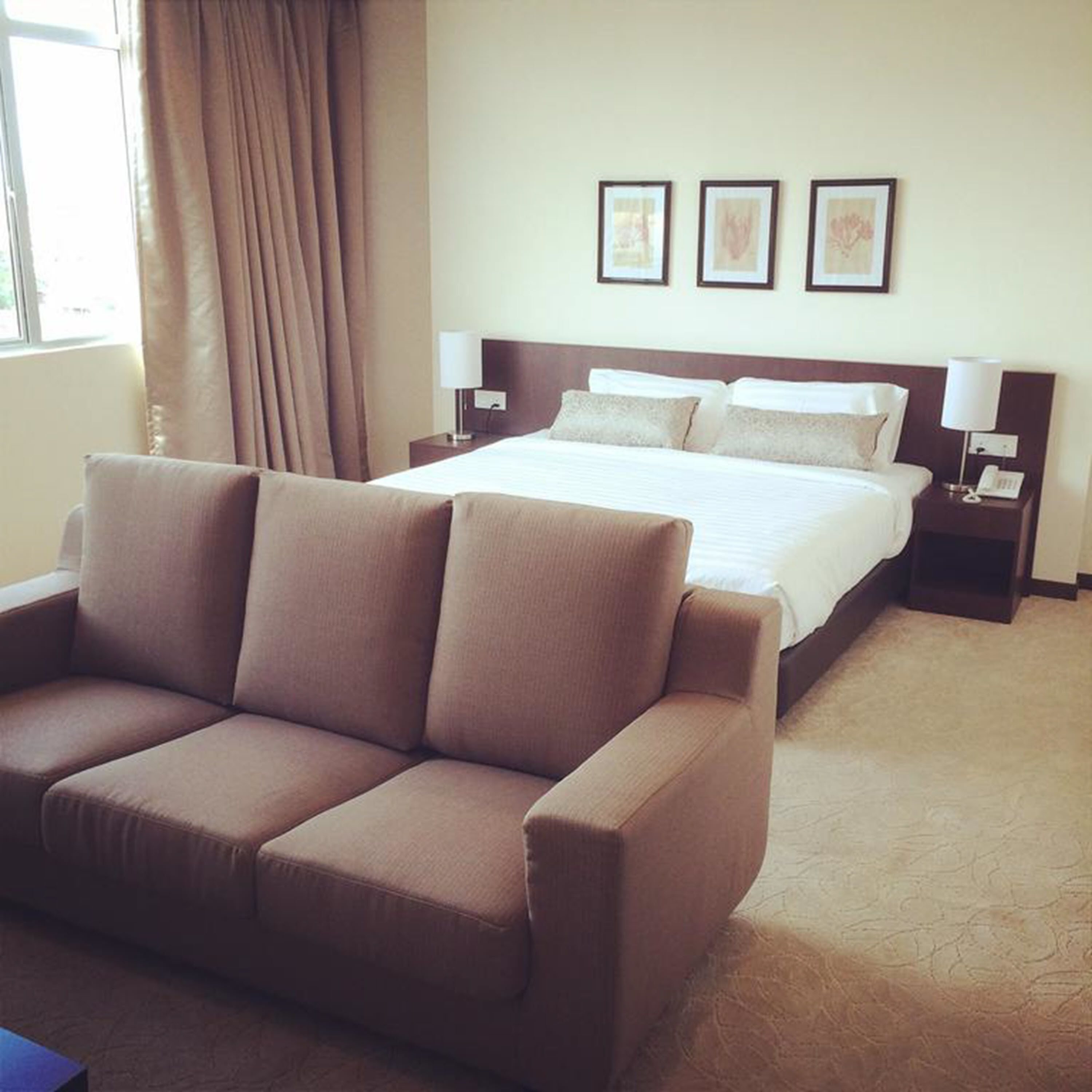 Une chambre d’hôtel avec un grand lit, un canapé, deux tables de chevet avec des lampes et trois tableaux encadrés au mur.