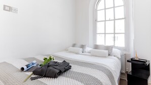 Une chambre d’hôtel minimaliste, dotée d’une grande fenêtre en arc de cercle, d’un lit soigneusement fait et d’une petite table de chevet.