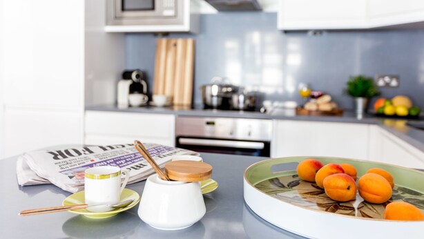 Une cuisine équipée d’un four à micro-ondes, d’une cuisinière et de divers ustensiles de cuisine. On y trouve une assiette de fruits et un journal sur le comptoir.