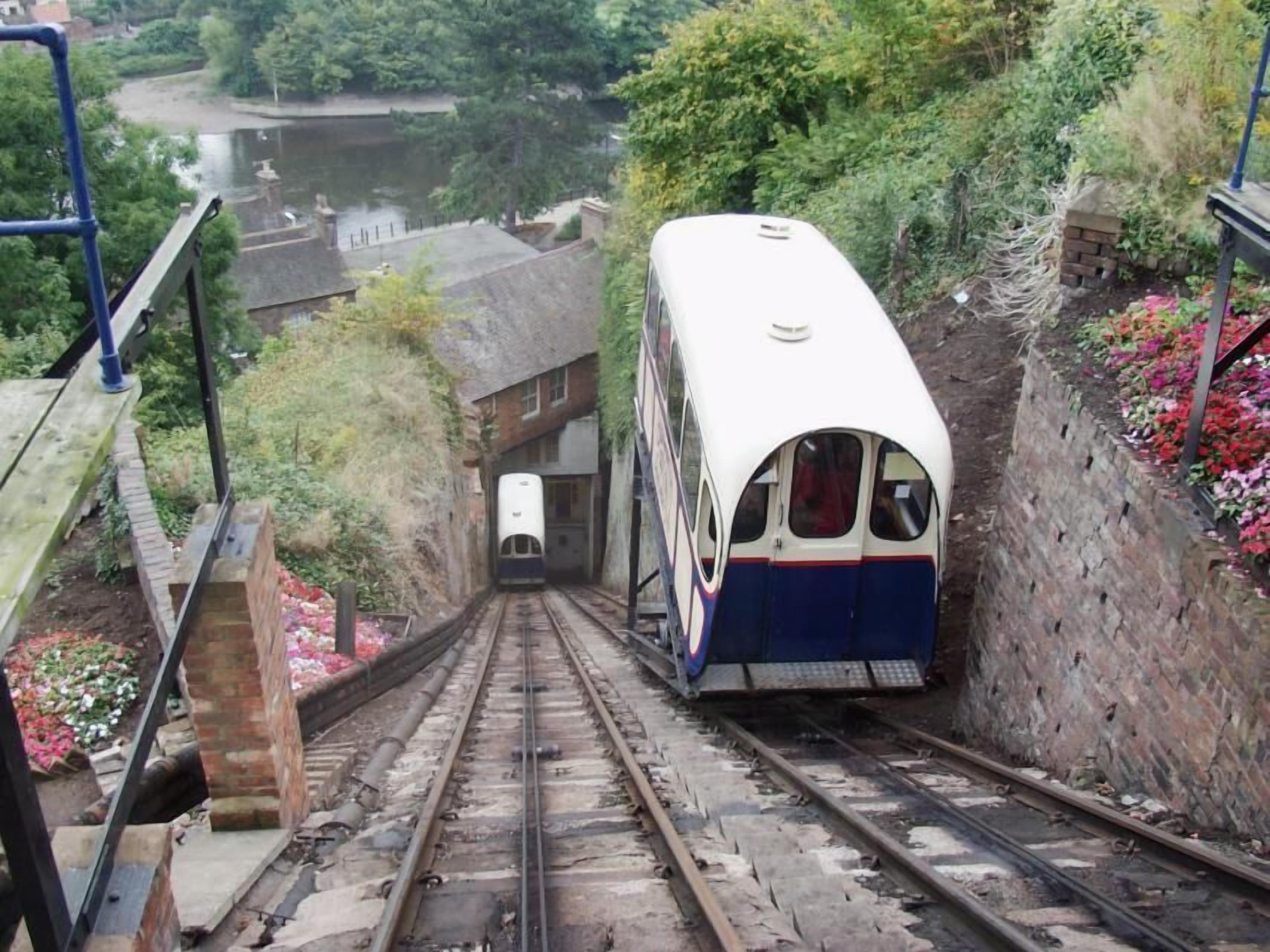 Een trein rijdt een steile rails af, omringd door groen en woongebouwen.