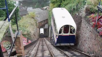 Een trein rijdt een steile rails af, omringd door groen en woongebouwen.