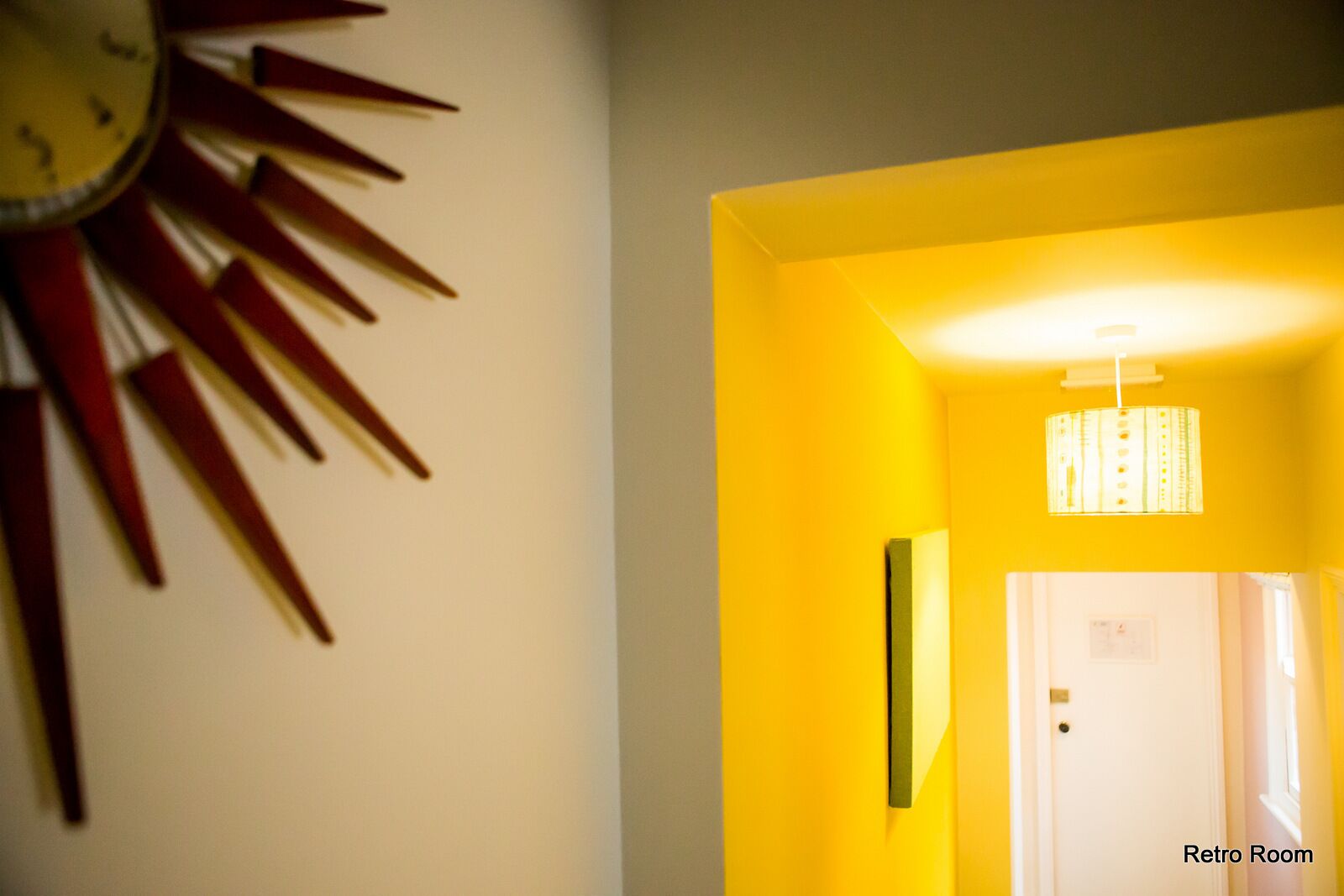 A hallway with a yellow wall and a clock with a sun-like design.