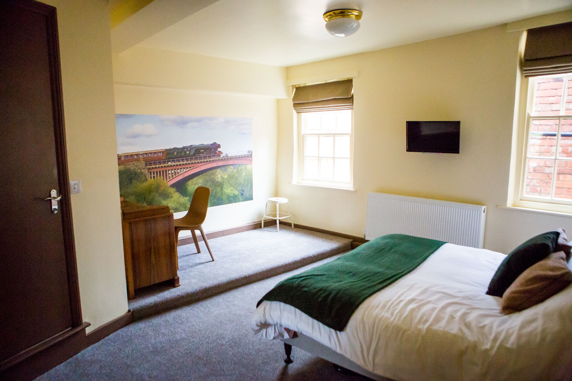 A bedroom with a bed, a desk, a chair, a window with a view of a bridge, and a television on the wall.
