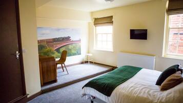A bedroom with a bed, a desk, a chair, a window with a view of a bridge, and a television on the wall.