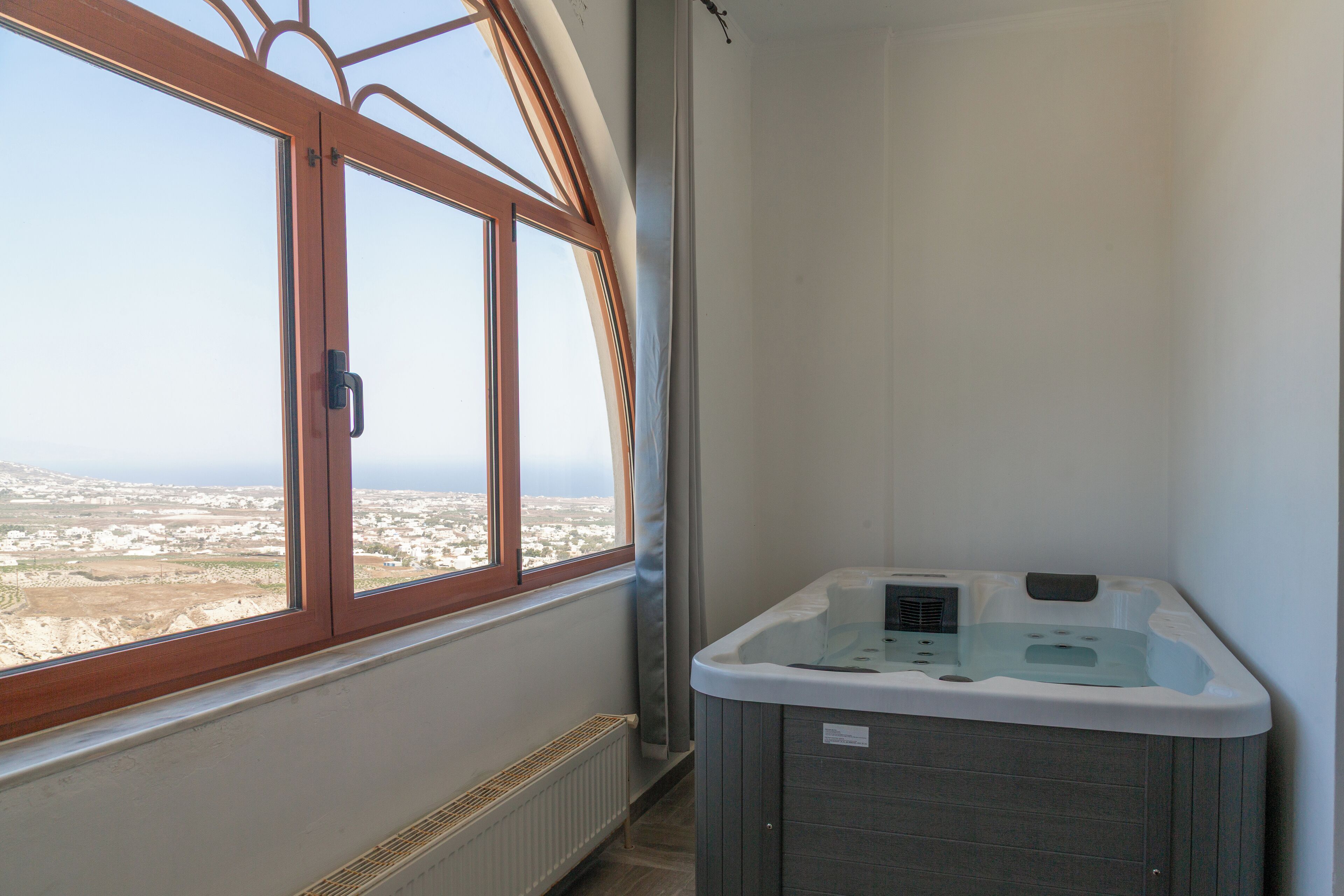 A room with a large window, a hot tub, and a view of a distant landscape.