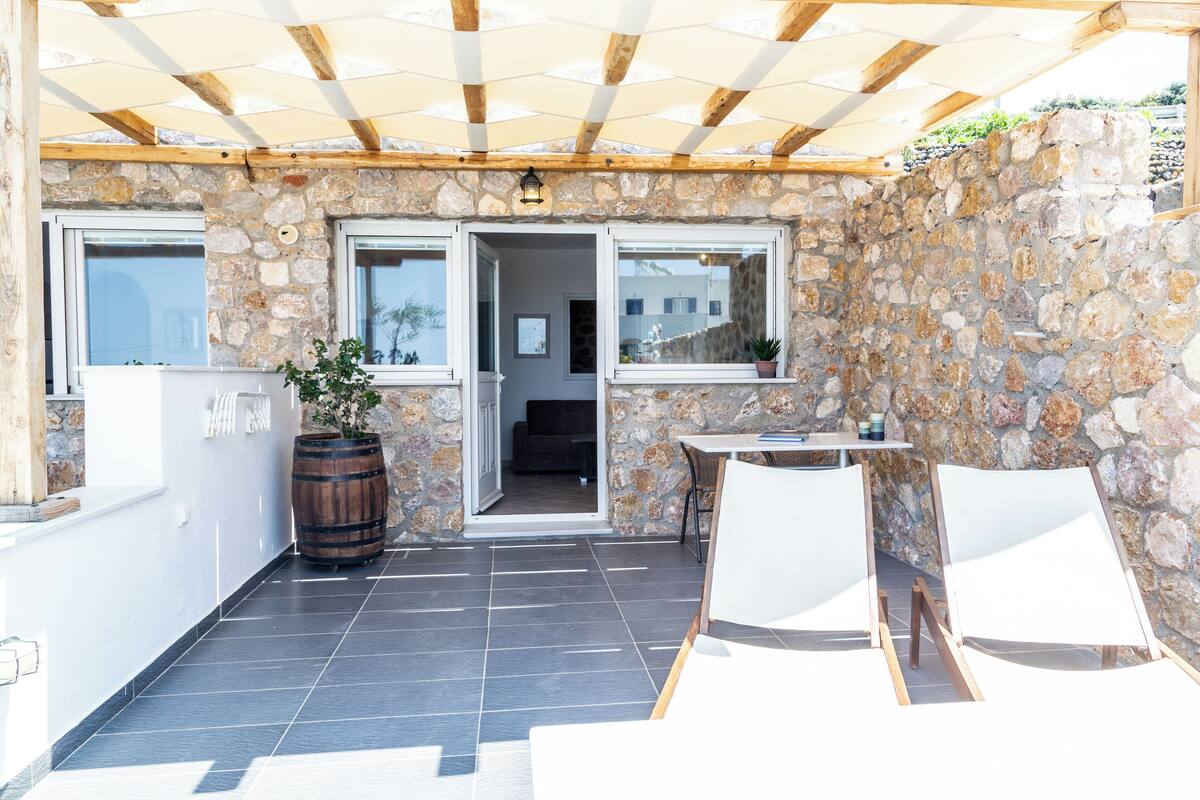 Un porche cubierto con paredes de piedra, techo de madera y vistas hacia la casa.