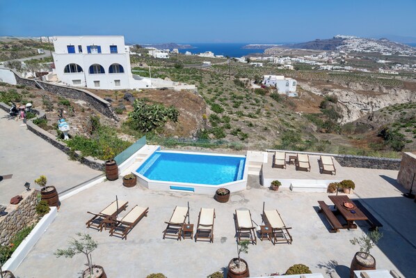 A rooftop pool with lounge chairs and potted plants, surrounded by white buildings and a view of the sea. - Aroma Cavas (Santorini)