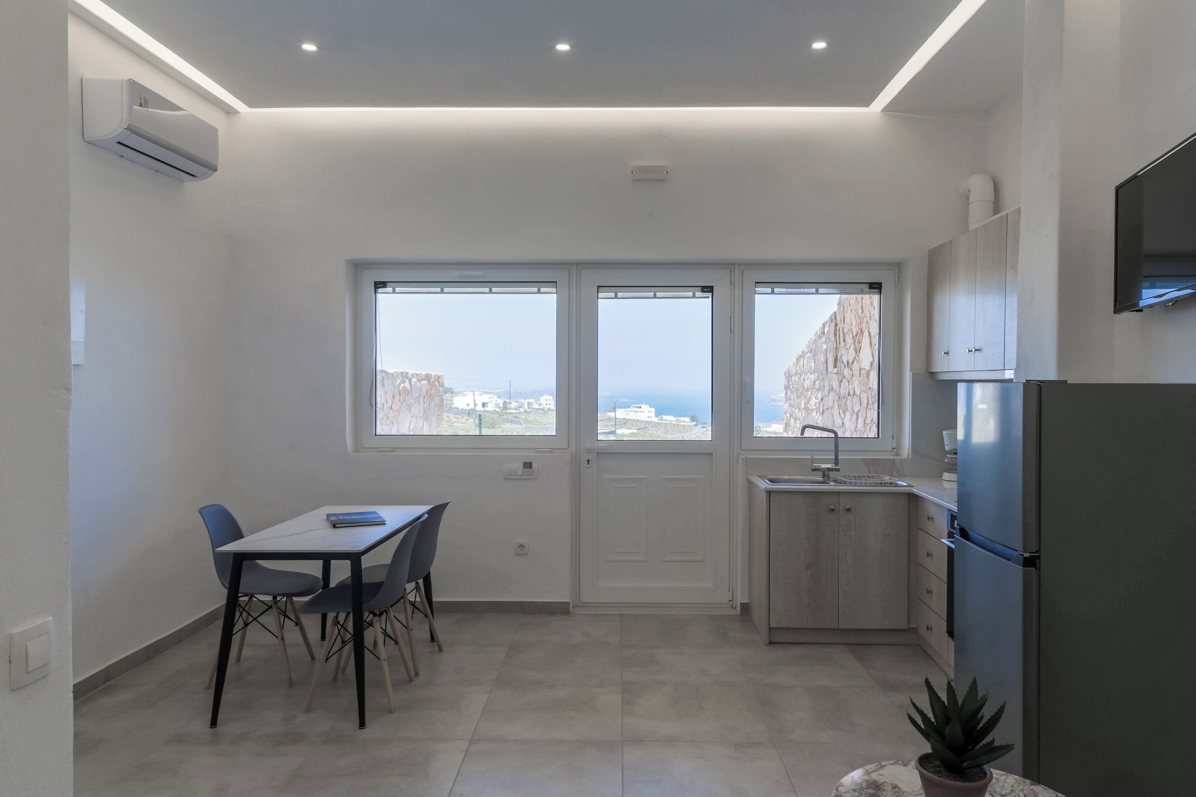 Una cucina moderna con frigorifero integrato, zona pranzo con tavolo e sedie, e ampie finestre con vista mare.