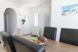 A dining area with a wooden table, black chairs, and a bowl of fruit. - Aroma Cavas (Santorini)