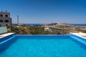 A swimming pool with a view of a coastal town and a mountain in the distance. - Aroma Cavas (Santorini)