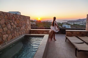 A pool area with stone walls, a view of the sunset, and lounge chairs. - Aroma Cavas (Santorini)