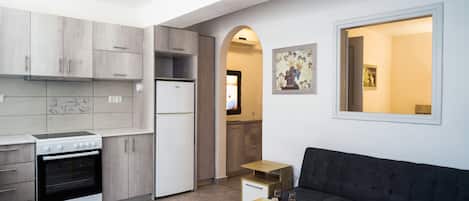 A compact kitchen with a stove, refrigerator, and wooden cabinets. There is a dark sofa and a small table with a glass top.