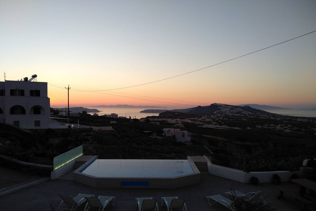 Zona de piscina con sillones de descanso y vista al mar al atardecer.