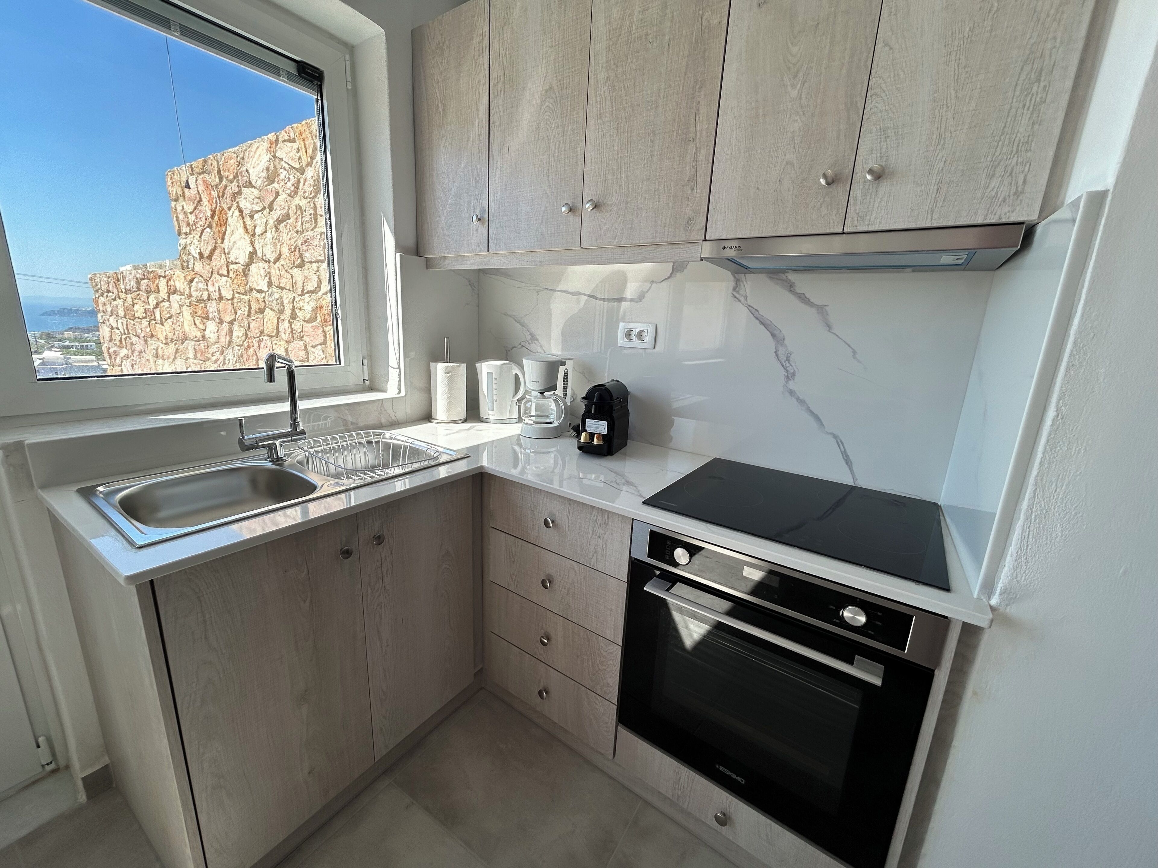 A compact kitchen with a stone wall, a sink, a coffee maker, and a stove.