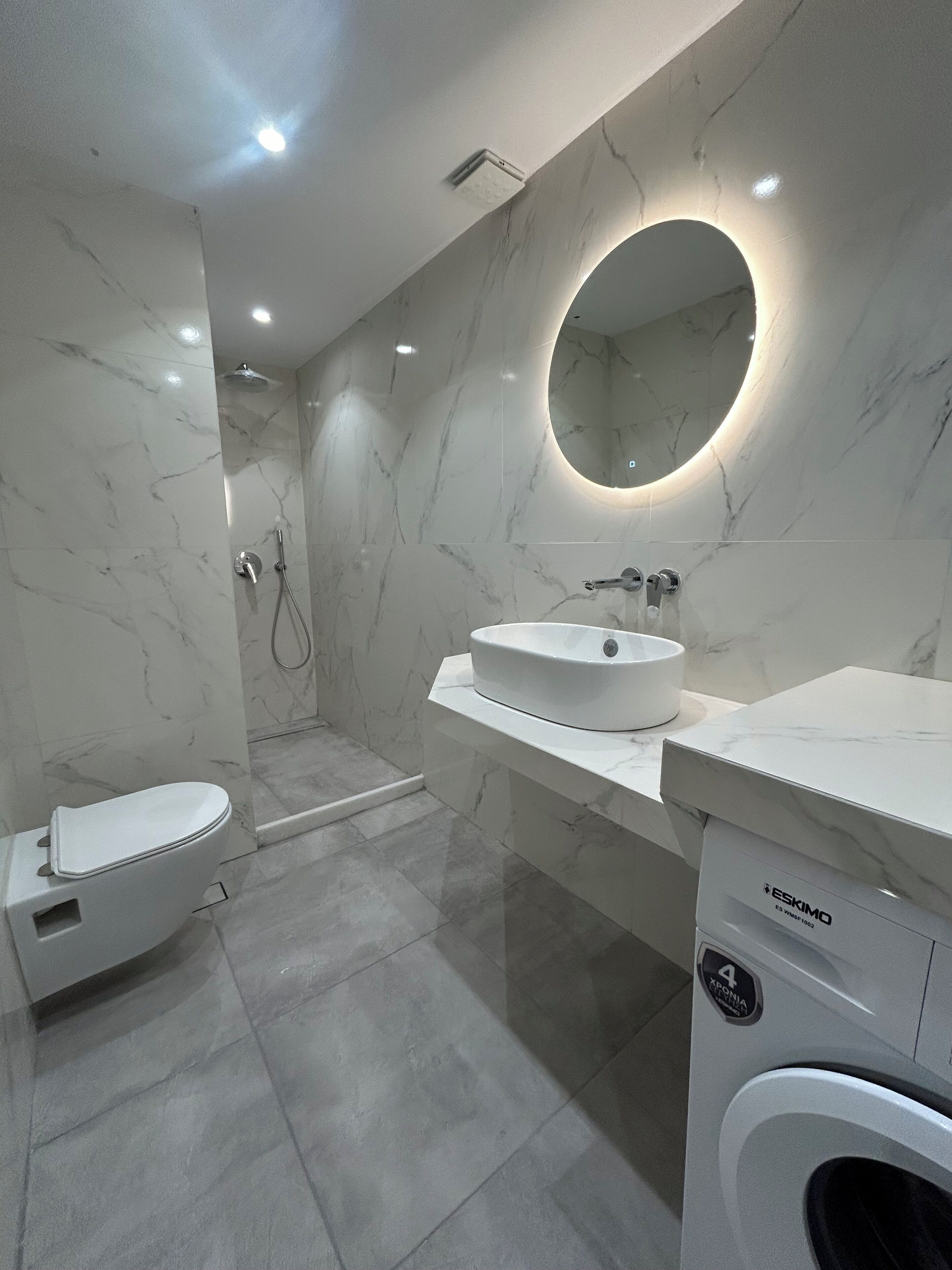 A modern bathroom with a white sink, a toilet, a shower, and a built-in washing machine.