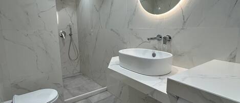 A modern bathroom with a white sink, a toilet, a shower, and a built-in washing machine.