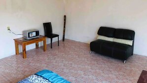 A room with a patterned floor, a black sofa, a wooden table with a device, and a black chair. - Mexica Apartment 20-30 min from the Airport (San Miguel Xalostoc)
