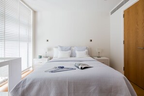 A bedroom with a bed, bedside tables, a wooden door, and a window with blinds.