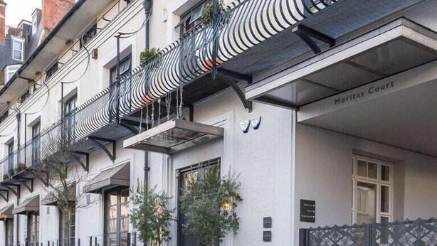 Un immeuble à la façade blanche, doté de balcons en métal noir et d’une enseigne indiquant « Meritas Court ».