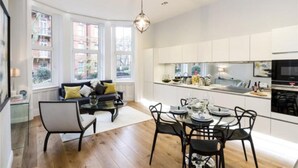 Una cocina moderna con gabinetes blancos, un comedor con mesa y sillas redondas, y ventanas amplias con vista a la ciudad.