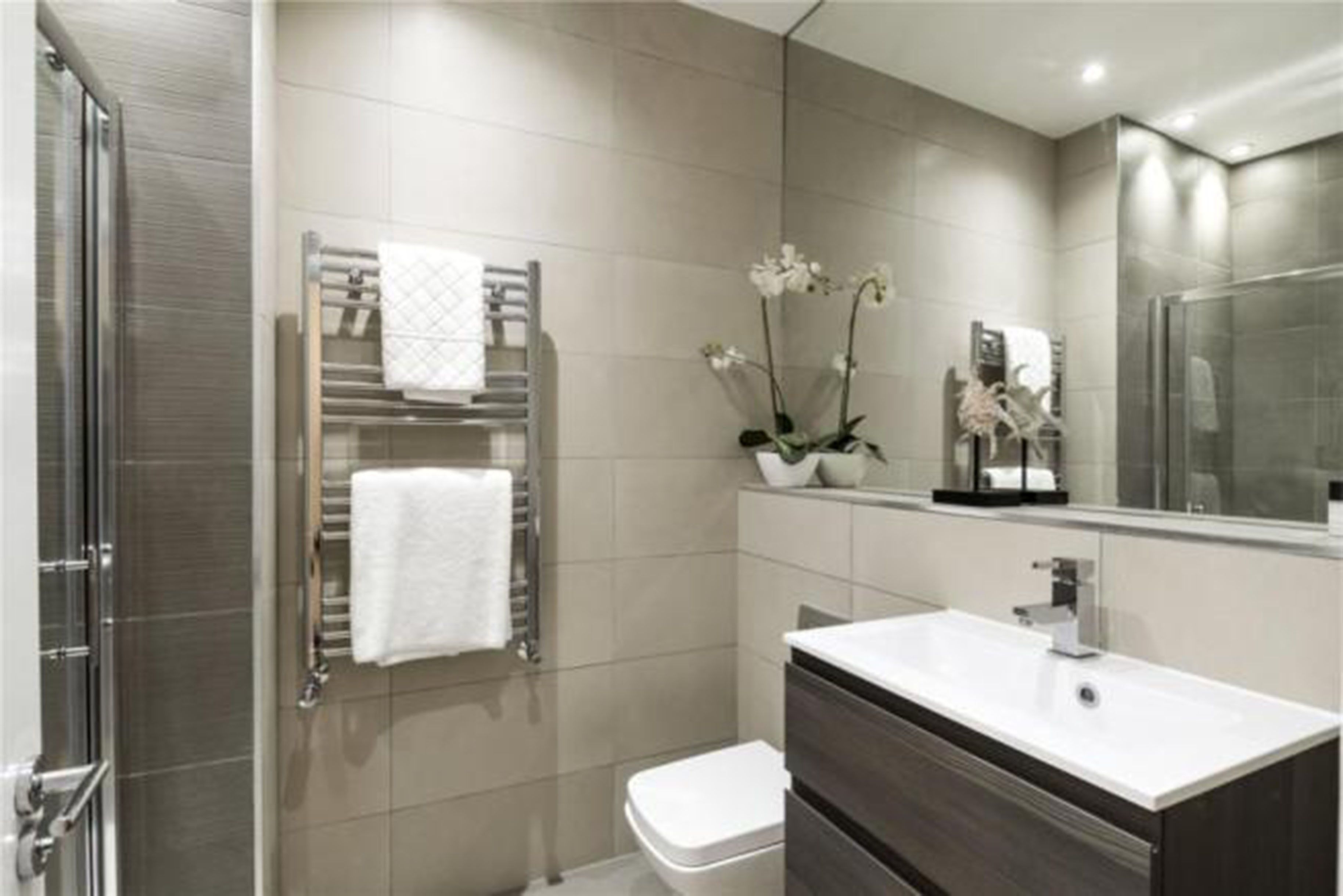 A modern bathroom with a glass shower enclosure, a white sink, and a towel rack with a white towel.