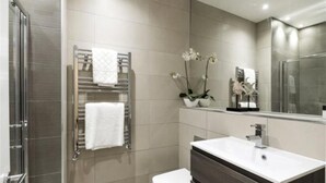 Un baño moderno con mampara de vidrio, lavamanos blanco y toallero con toalla blanca.