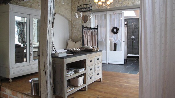 Une pièce rustique avec des poutres apparentes, une commode en bois, un lustre et une vue sur une salle de bain avec douche.