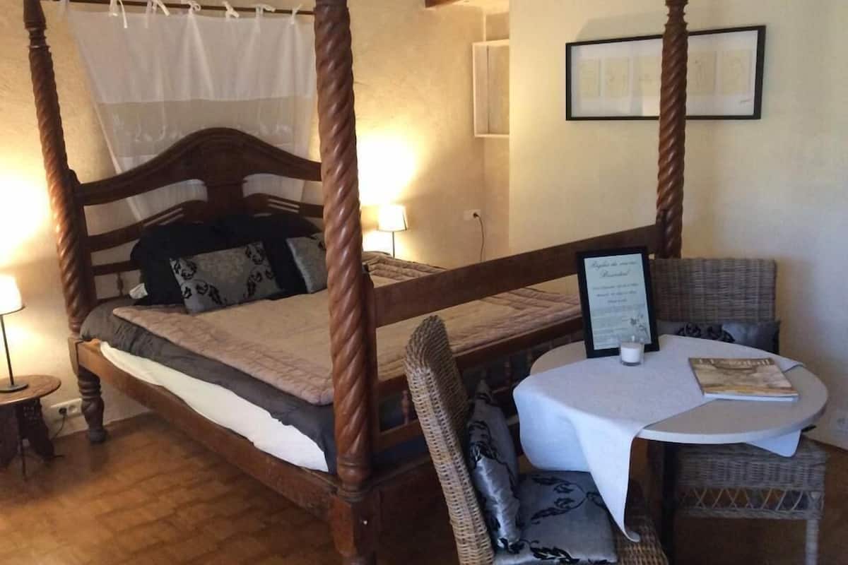 Een hemelbed met baldakijn, een ronde tafel met een boek, en een rieten stoel.