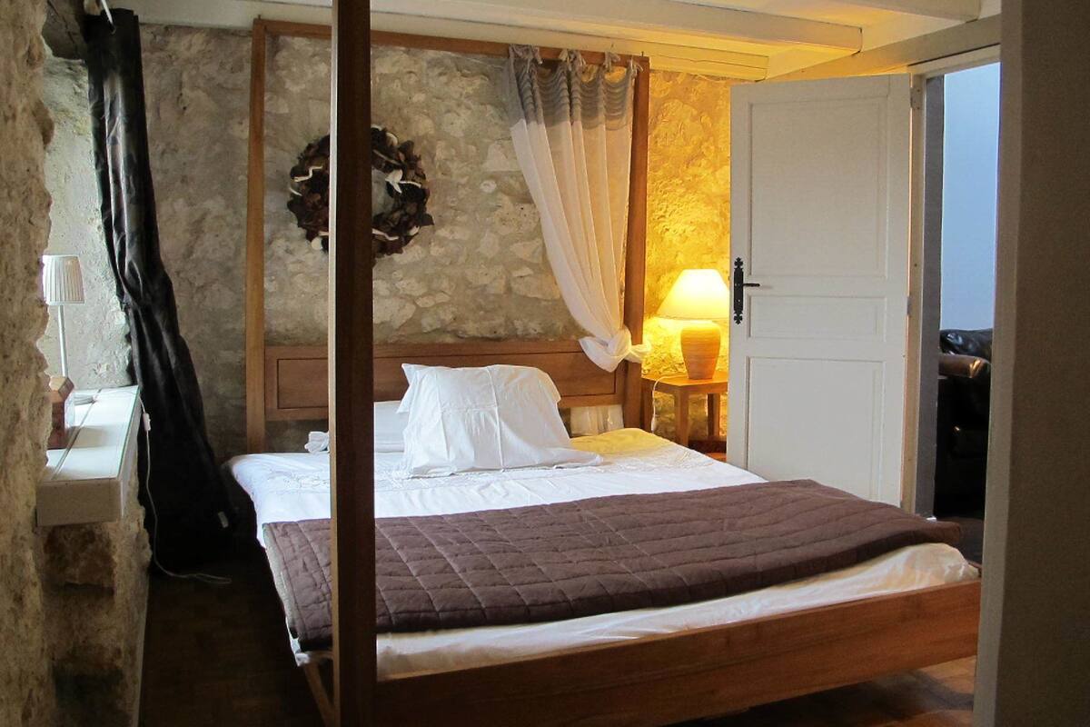 Een slaapkamer met een bed, nachtkastje, lamp en een stenen muur.