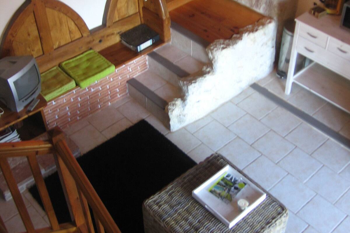 Een gezellige kamer met een open haard, een houten bankje, een rieten poef en een televisie op een houten dressoir.