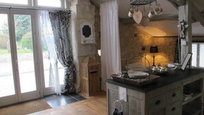 Une cuisine rustique avec un îlot central en bois, un luminaire suspendu et une vue à travers les portes vitrées.