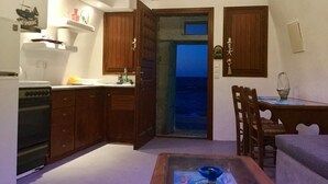 Una cocina compacta con armarios de madera, horno integrado y vista al mar a través de un ventanal abierto.