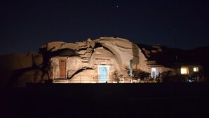 Una estructura tipo cueva con una puerta azul, un pequeño edificio adyacente con luz y un área cercada.