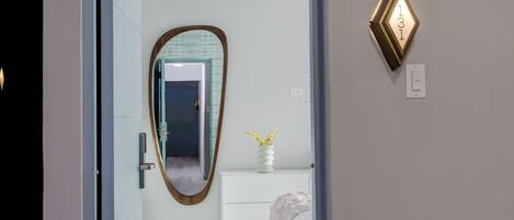 Une chambre d’hôtel moderne avec un grand miroir, une table de chevet ornée d’un vase et un luminaire fixé au mur.