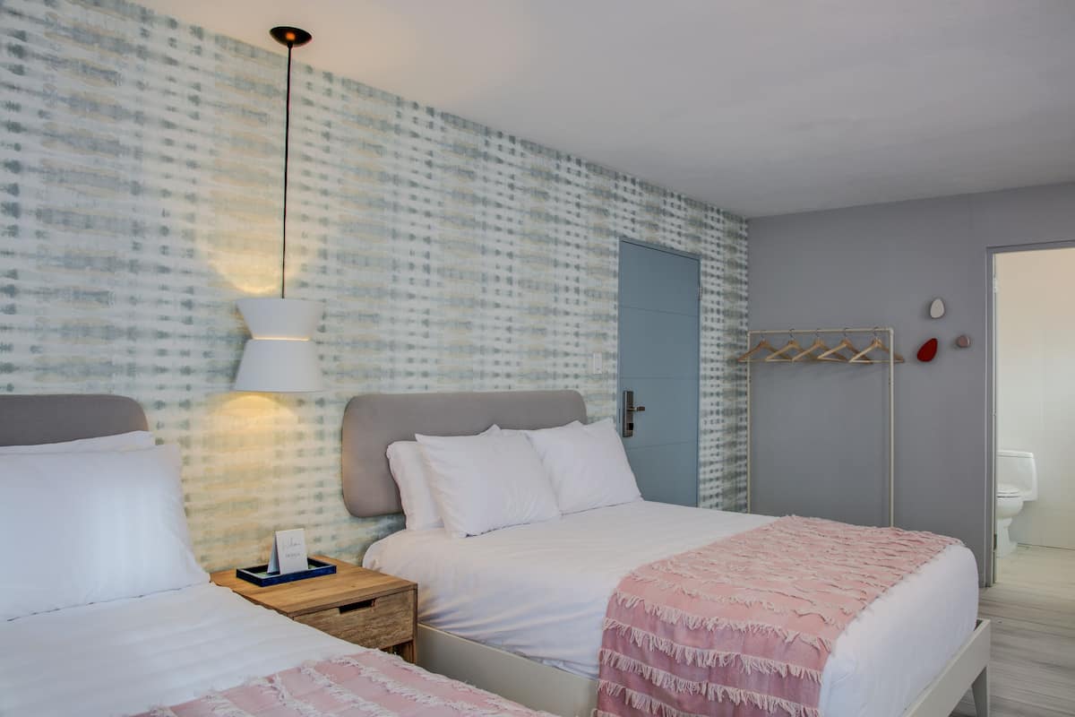A bedroom with two beds, a bedside table, a lamp, a wardrobe, and a bathroom with a toilet.