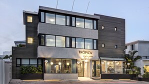 A modern two-story hotel named Tropica Beach Hotel with large windows, a visible restaurant, and outdoor seating. - Trópica Beach Hotel (San Juan)