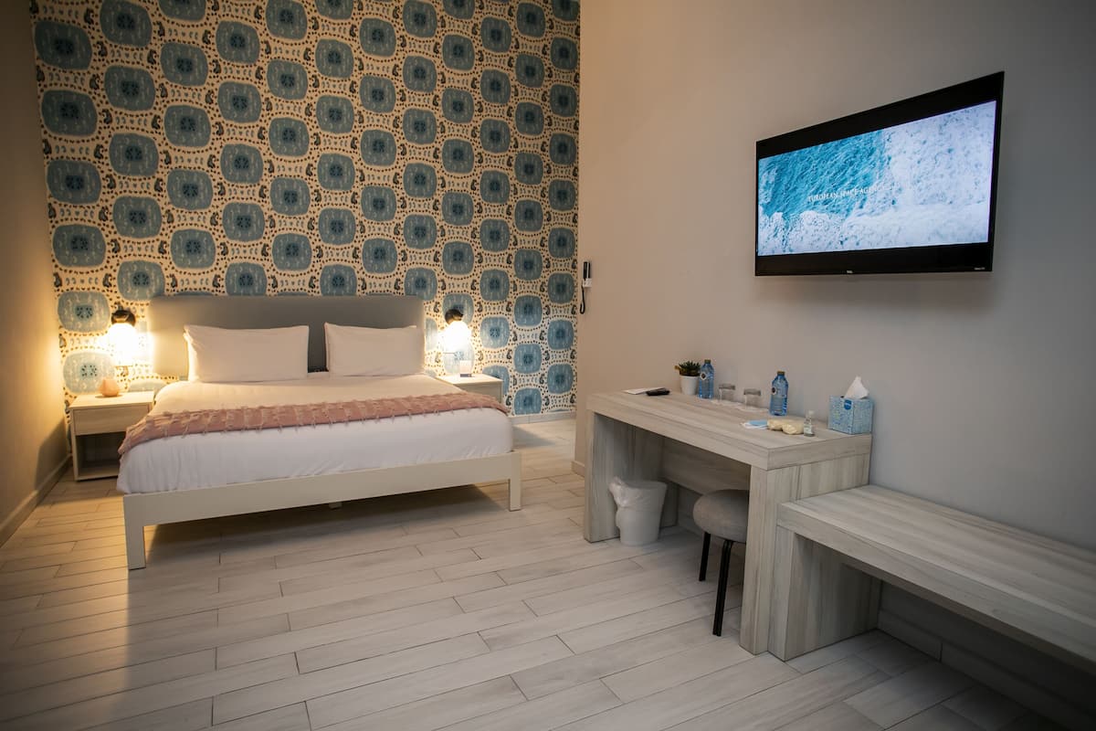 A modern hotel room with a bed, bedside tables, a desk, and a TV on the wall.