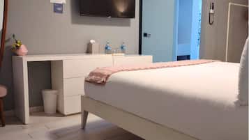 A modern bedroom with a bed, a desk, a television, and a bathroom.