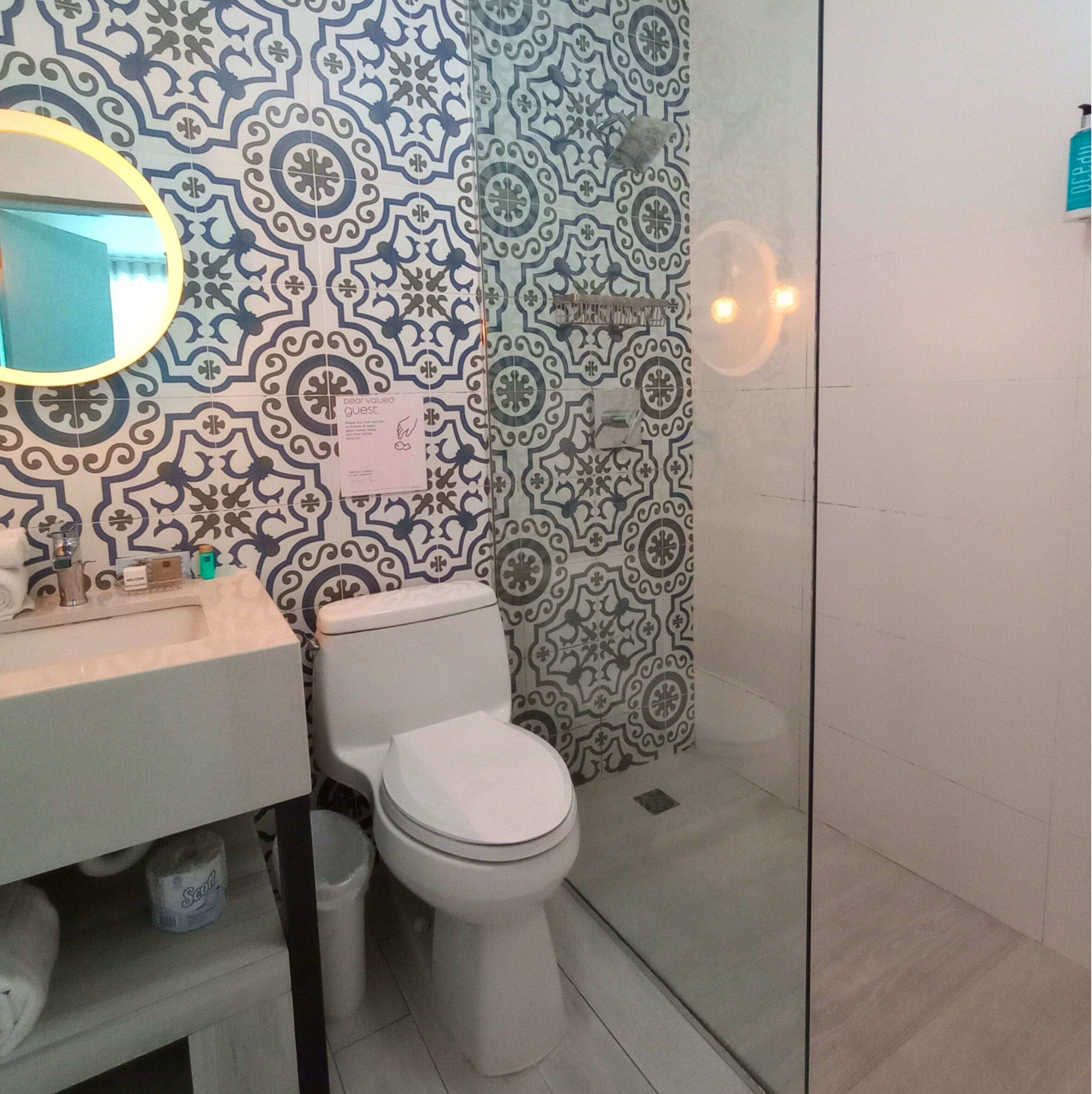 Ein Badezimmer mit einer Wand aus gemusterten Fliesen, einer Toilette, einem Waschbecken und einer Duschkabine.
