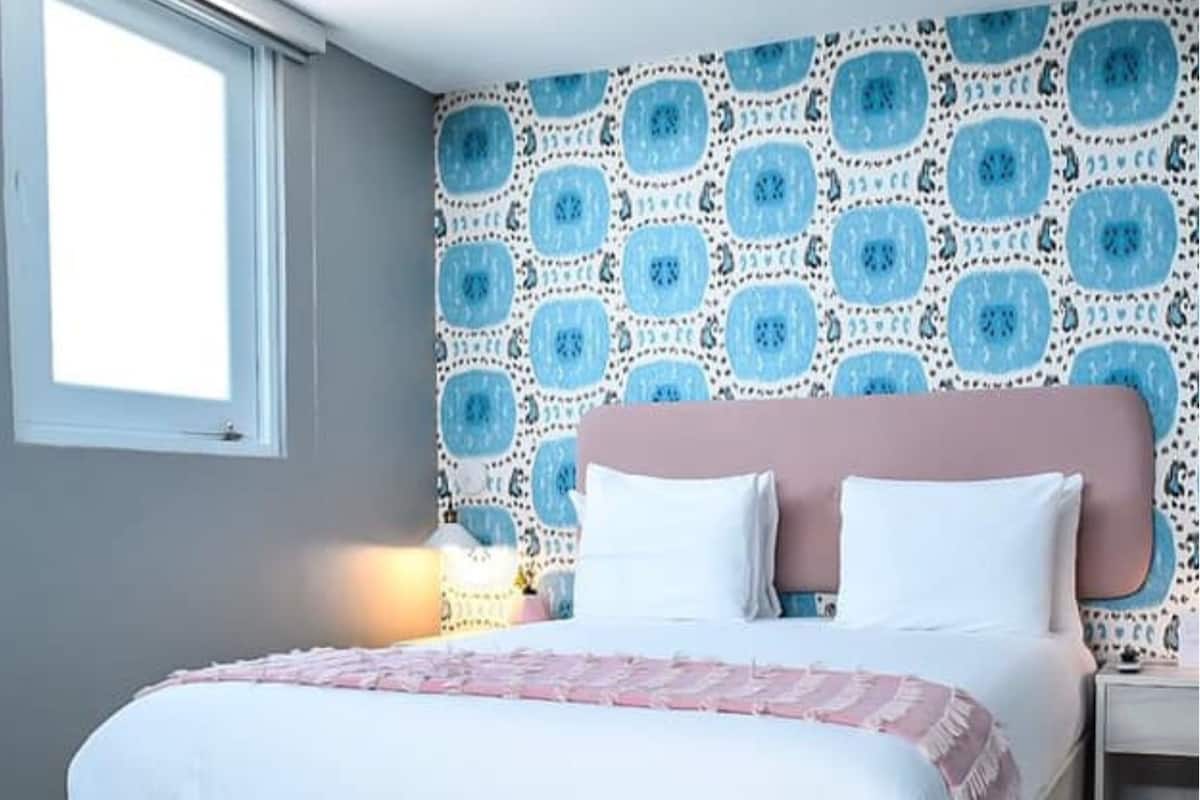 A bedroom with a bed, a nightstand, a wall with a patterned wallpaper, and a window.