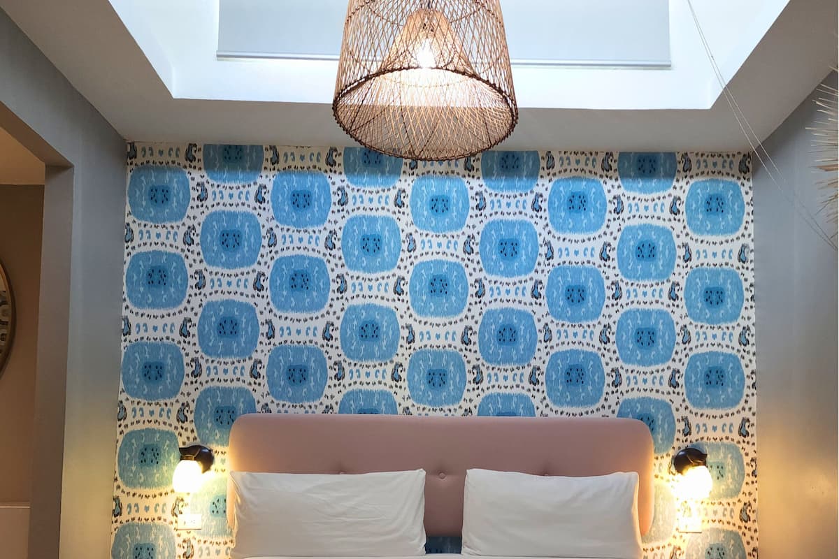 A bedroom with a bed, two bedside lamps, a patterned wall, and a skylight.