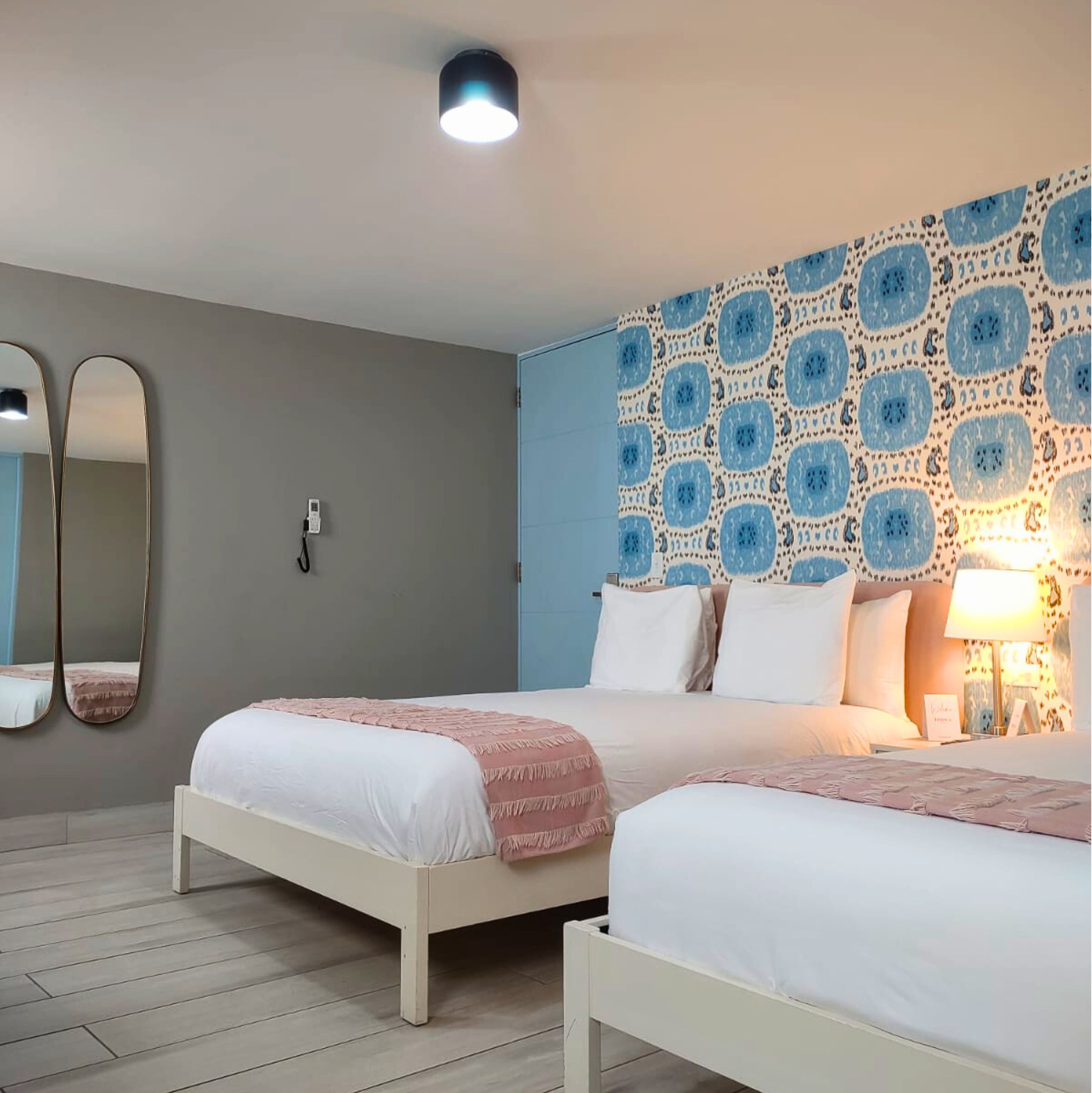 A bedroom with two beds, a mirror, a wall-mounted light, and a patterned wall.