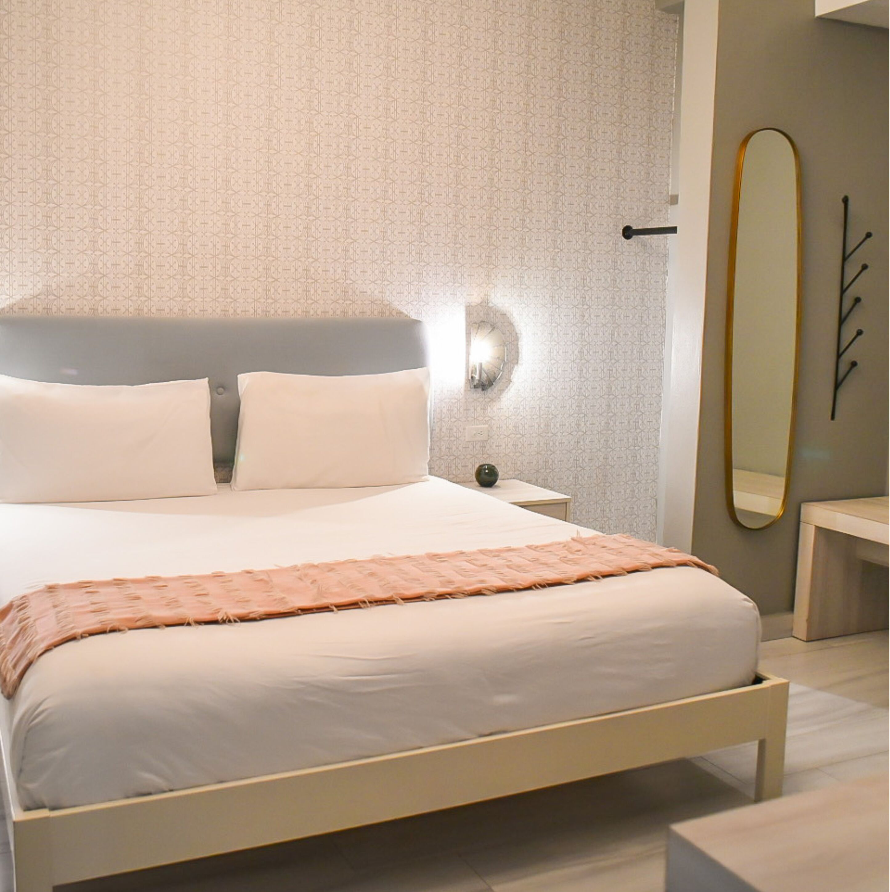 A modern bedroom with a bed, bedside tables, a wall-mounted light, and a mirror.
