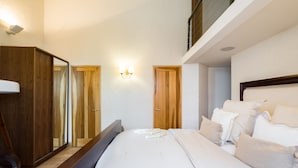 A bedroom with a large bed, wooden wardrobe, and a mirror. - One Palace Gate (London)