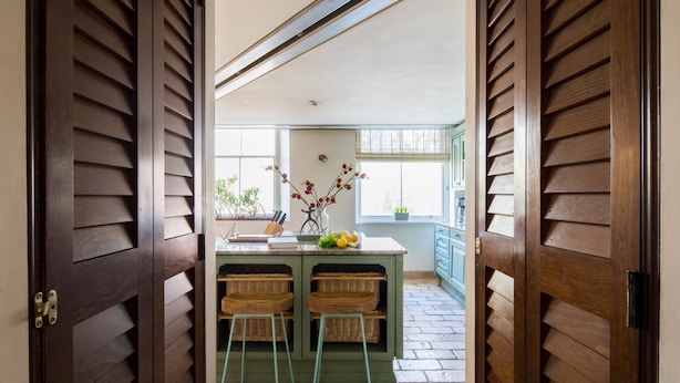 A kitchen with wooden shutters, a central island with stools, and a window with a view. - One Palace Gate (London)