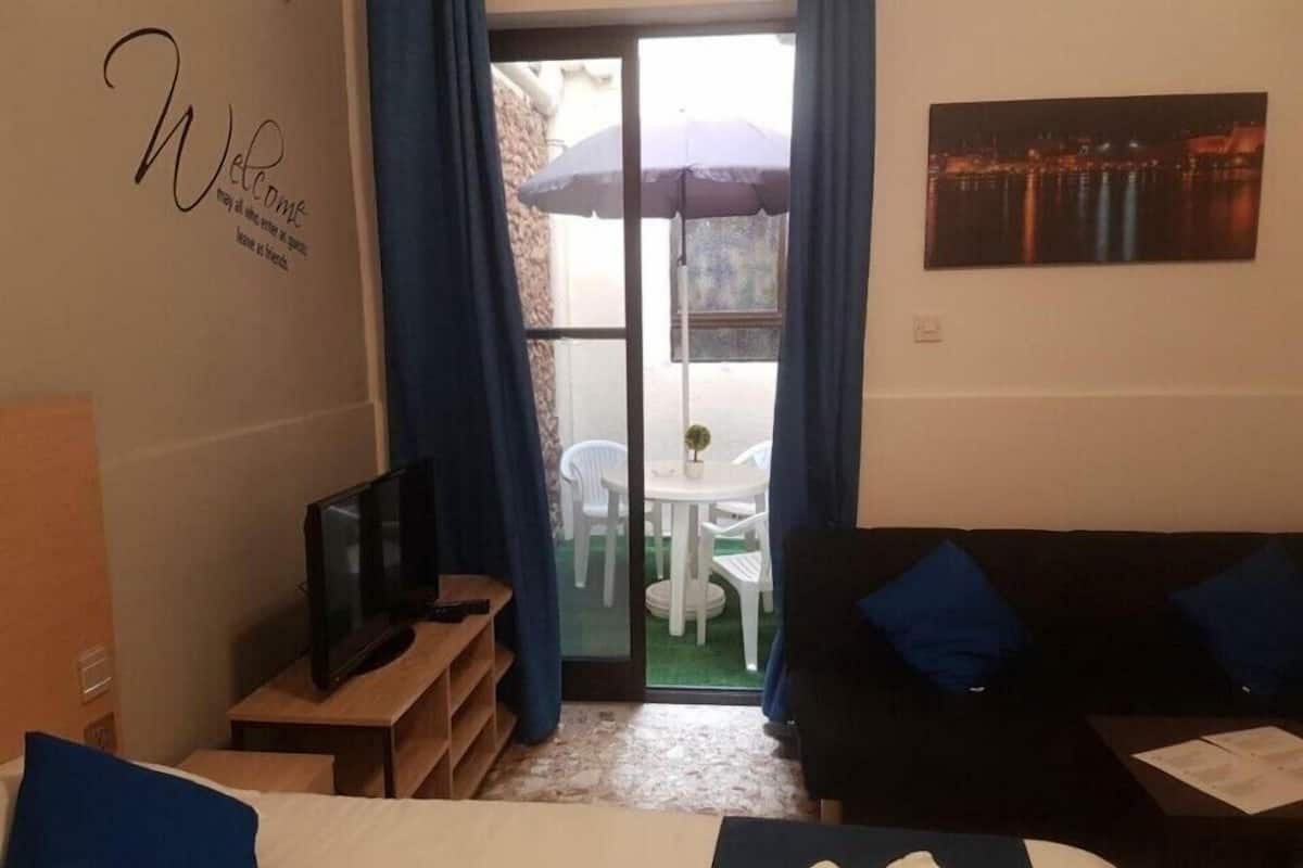 Habitación de hotel con cama, televisor, sofá, una mesita y un balcón con mesa y sillas.