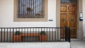 A building facade with a large wooden door, a window with decorative iron bars, and a small bench with potted plants. - Le Malte House St Julians (St. Julian's)